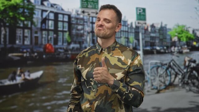 Man in camouflage shirt gives thumbs up and winks on a street by a canal with parked bicycles, soldier attire visible; pride duty.