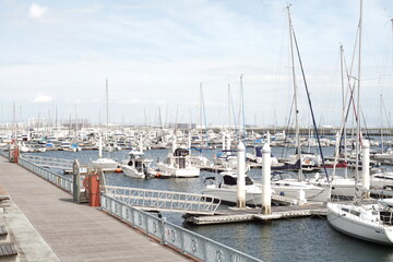 Fototapeta premium Scenic view of numerous yachts and cruisers moored at a marina with a wooden broadwalk under a blue sky.