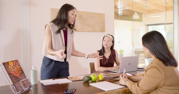 Asian women receiving prints as lead leaning forward, showing samples for review with laptop, fruit
