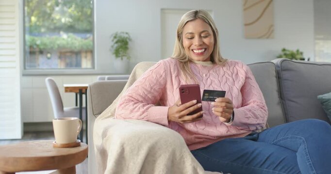 African American woman wearing pink sweater on sofa, using phone during checkout verifying card