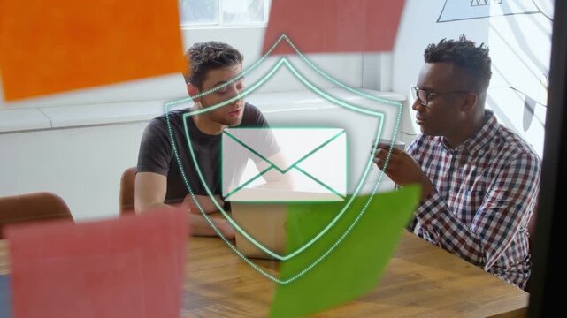 Two men working at laptop talking tech causing teal particles forming shield over it securing mail