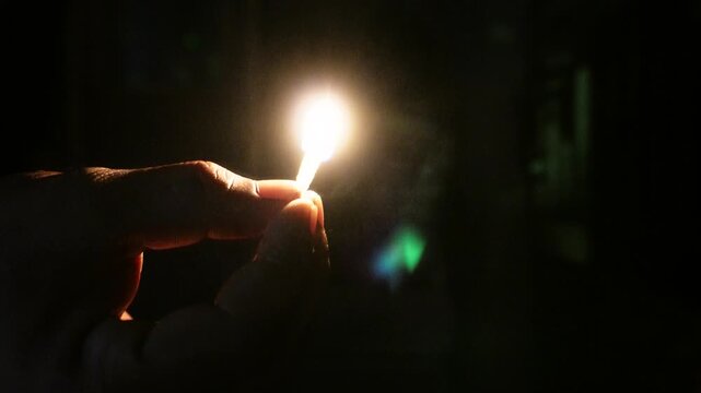 Hand Holding Lit Matchstick against Dark Background