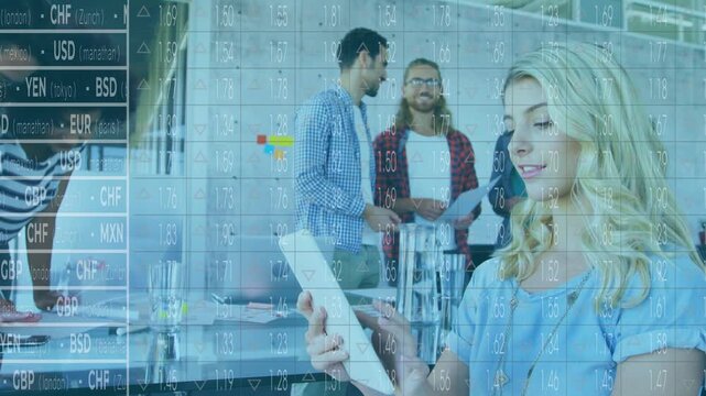 Seated woman tapping tablet and activating currency overlay while colleagues reviewing finance