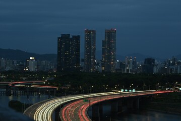 Long exposure of car light trails on a city road at night with modern skyscrapers. © GEONHEE