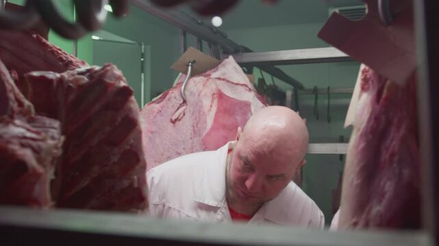 Production control man supervisor inspects, controls beef, production line of raw meat factory in industrial cold room storage refrigerator. Quality control. Male inspector checks freshness of meat