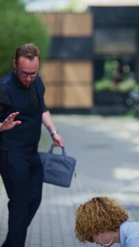 A man helps a woman collect her scattered documents after an accidental outdoor encounter. This moment illustrates helpfulness and a potential business partnership.
