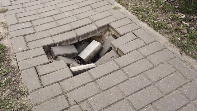 Close up view of significant damage to sidewalk, multiple gray rectangular paving blocks fallen into ground depression, representing poor infrastructure maintenance and need for repair