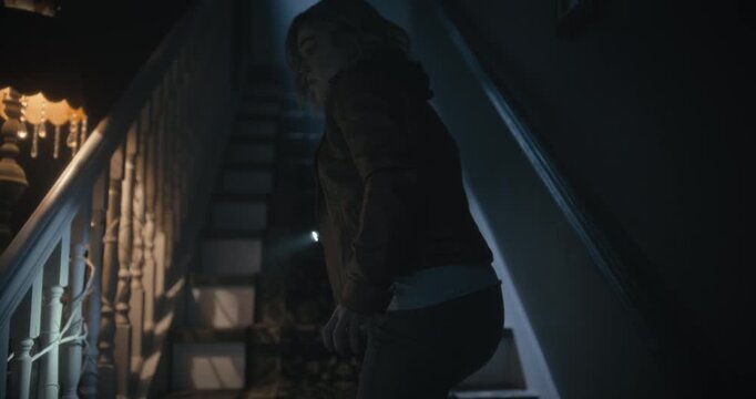 Lone young woman with flashlight walking on steps of scary, haunted house - steady cam shot