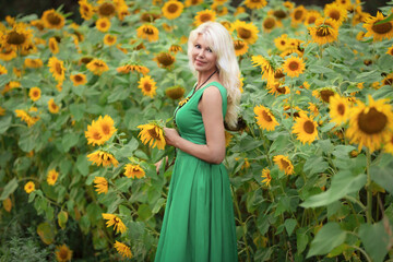 Naklejka premium Beautiful mature blonde woman holding sunflower in blooming summer field