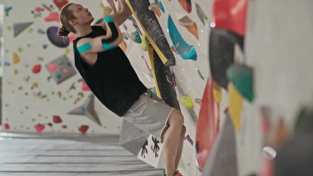Young male athlete with kinesiology tape climbing indoor bouldering wall and falling down. Video suitable for sports marketing, fitness apps, or physical therapy content