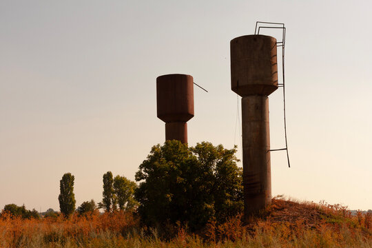 Two old concrete water towers stand tall against a hazy sky in a rural landscape