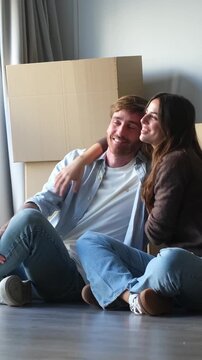 Happy young caucasian couple sitting on the floor of their new home, surrounded by cardboard boxes, dreaming about their future together and enjoying the moment of relocation