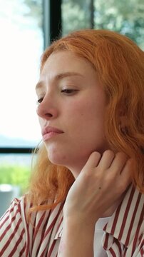 Closeup of a contemplative young redhead woman with a serious and pensive expression, feeling sad and thoughtful while sitting indoors, lost in her memories and dealing with stress