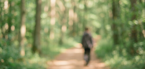 Fototapeta premium A blurred figure walking along a forest path surrounded by green trees, creating a serene and peaceful atmosphere in nature.