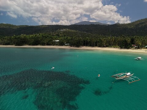 Aerial view of outrigger boats and paddleboards on turquoise water at Batchawan Beach in Puerto Princesa Palawan with sandy shore and forested hills