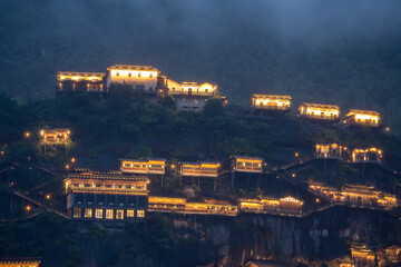 Fototapeta premium Traditional buildings with glowing lights stand on the cliffs of Wangxian Valley Scenic Area in Jiangxi China at night