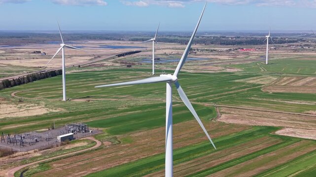 Aerial view shows windmills standing in a field near a river and ocean in Nova Scotia. The landscape features green fields and open space on a clear day