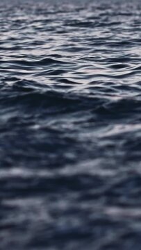 Close-up perspective of dark blue water surface with small waves and ripples reflecting subtle light. Image conveys peaceful and tranquil mood, suitable for abstract background or nature theme project