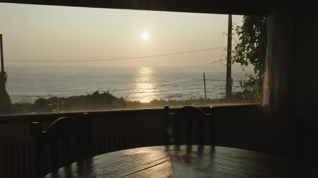 Breathtaking sunset view over the ocean framed by a dining room window, casting a warm, golden glow across the rustic wooden table and creating a serene, contemplative atmosphere of quiet reflection.