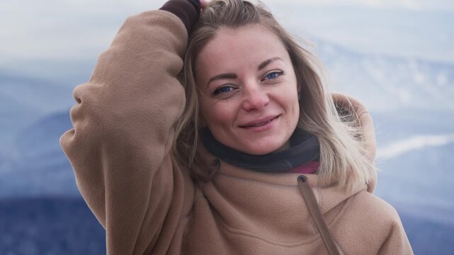 Portrait of a beautiful girl will fix her hair in winter. Beautiful big blue Eyes, Wind blowing on Blonde Hair. Happy skiing. Dressed in a hoodie. Travel to winter resort, adventure. Slow motion