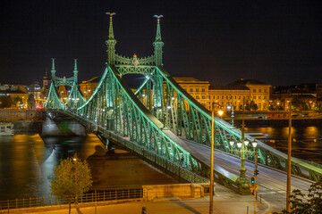 Fototapeta premium Illuminated Liberty Bridge and Main Building of University of Economics at night over Danube