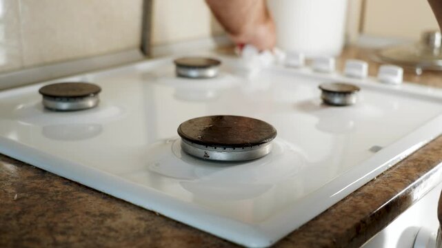 Man cleans white gas range burners and surface in kitchen