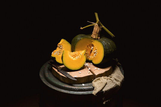 Green pumpkin with cut slices on wooden barrel in dark moody lighting. Autumn still life with squash and rustic texture