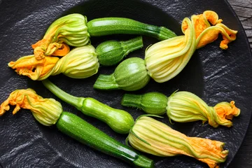 Fresh zucchini and blossoms arranged on dark plate, organic vegetables with edible flowers, cooking ingredient concept. Green squash and yellow blossoms top view © Ivan Kmit