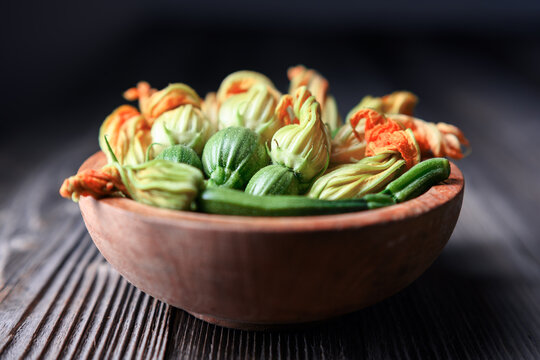 Fresh zucchini blossoms with small squash in bowl, edible flowers for cooking, culinary concept. Yellow blossoms and green squash close-up, soft light, gourmet ingredient