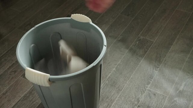Close-up view of hand removing used, full dust bag from vacuum cleaner, preparing to discard it into a grey plastic trash can, emphasizing everyday cleaning and maintenance duties.