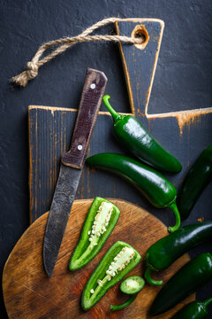 Black jalapeno with knife on rustic wooden cutting board close up. Green mexican jalapeno hot peppers