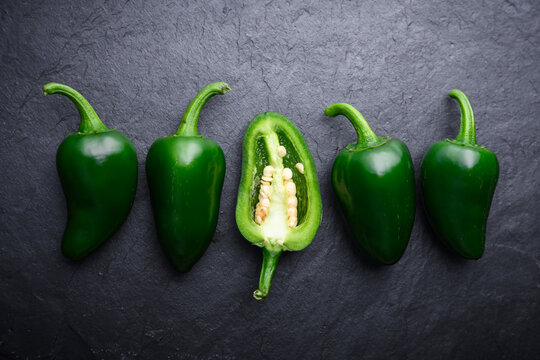 Arrangement of jalapeno peppers with sliced half placed among whole pieces. Fresh green chili on dark stone surface top view