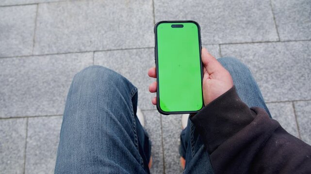 A man stands on a bustling street, showcasing his smartphone. The close-up reveals the gadget as he interacts with it, capturing the essence of technology amidst the urban hustle