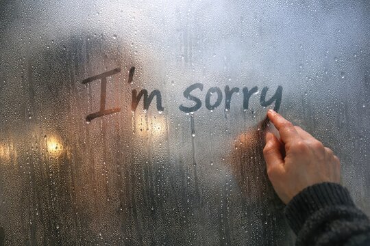 A person writes an apology message on a cold and frosty window