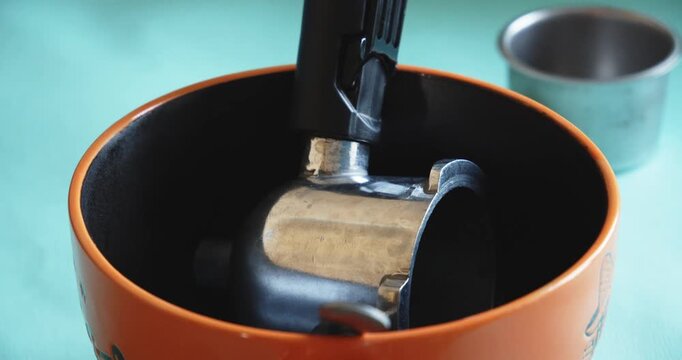 The metal holder of a carob coffee maker lies at the bottom of an orange bowl while soaking and cleaning from deposits