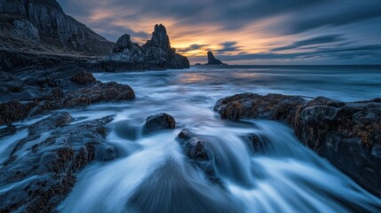 Obraz premium Dramatic coastal sunrise over rocky shore. Ocean waves cascading over rocks. Misty atmosphere