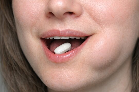 A woman holds a pill in her mouth, ready to take it
