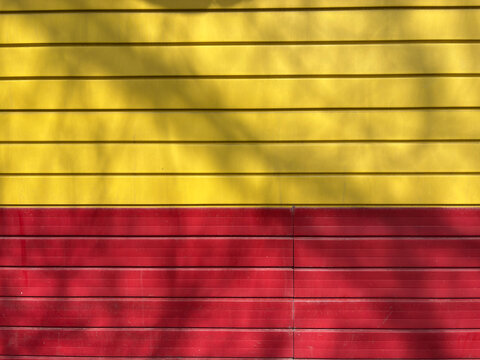 Textured yellow and red wall with horizontal stripes and leaf shadows