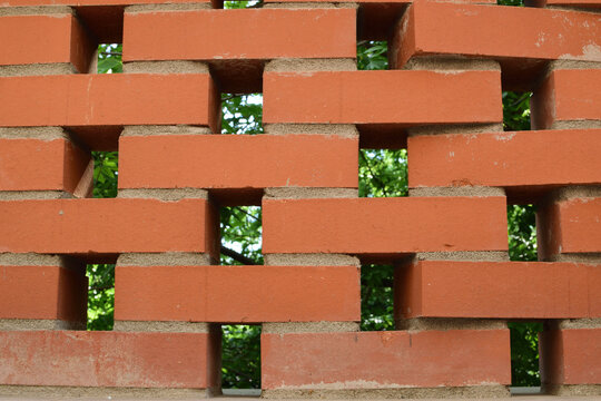 Decorative perforated brick wall pattern with green foliage in the background.
