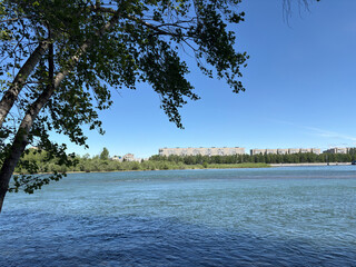 River flowing past trees and apartment buildings on shore © Qazy