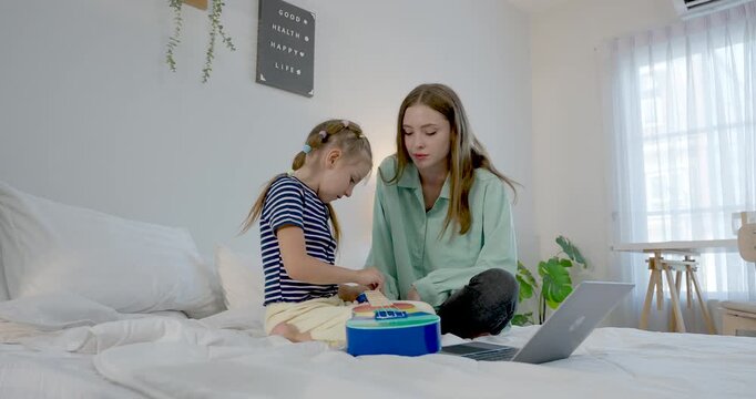 Caucasian mother helps preschool girl press colorful buttons on blue learning toy beside laptop, counting practice, patient coaching, homeschool playtime, nurturing family care, skill growth