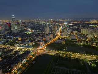 Naklejka premium Night aerial view of Ho Tung Mau Street in Cau Giay District with illuminated traffic corridors and dense Hanoi skyline.