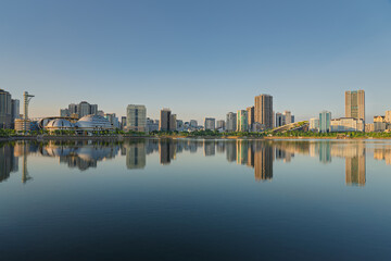 Obraz premium Wide panoramic skyline around Cau Giay Lake mirrored across still water under clear evening light in Hanoi.