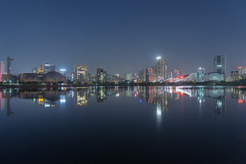 Fototapeta premium Night skyline of Cau Giay Lake features illuminated buildings and colorful reflections across calm urban waters in Hanoi.