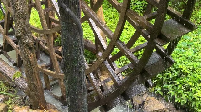 Wooden water wheel spinning in a small stream. Old machinery for generating energy in the countryside. Traditional mechanism for milling grain. Concept renewable power and nature. Watermill close up.
