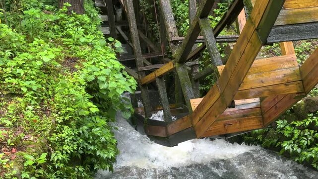 Wooden water wheel spinning in a small stream. Old machinery for generating energy in the countryside. Traditional mechanism for milling grain. Concept renewable power and nature. Watermill close up.