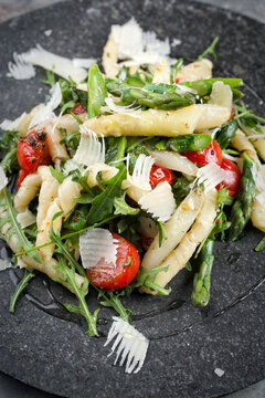 Cold vegetarian pasta noodle salad with green and white asparagus tips, arugula, fresh tomatos and parmesan served as close-up on a black stone plate