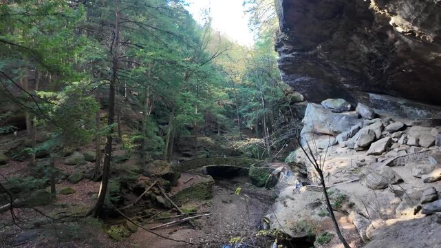 View of the historic stone bridge and massive rock overhang surrounded by lush forest at Hocking Hills State Park in Logan, Ohio, United States.