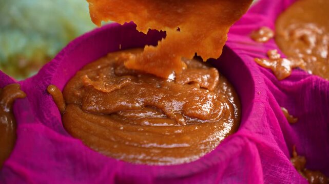 View of traditional brown sweet paste being poured and filtered through a bright pink cloth during food preparation in Natore, Rajshahi Division, Bangladesh.