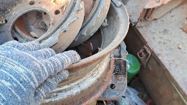 Gloved hand holding large rusty brake drum in scrap metal pile